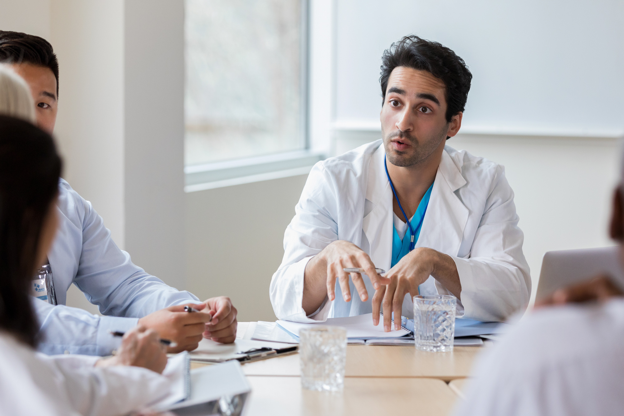 Handsome male doctor has serious look while conversing with other doctors at a conference table